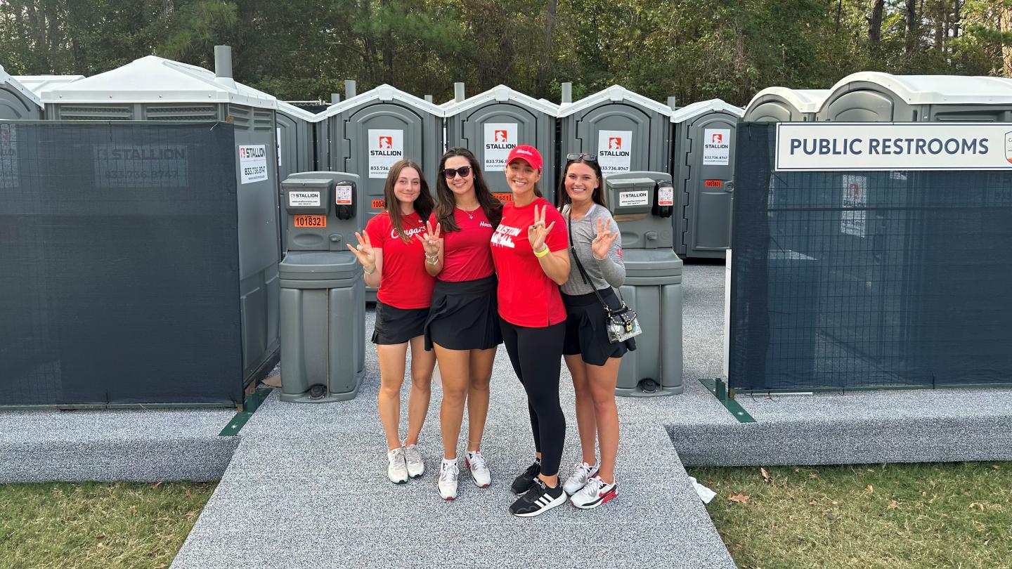 Ladies smiling and waving in front of portable toilets